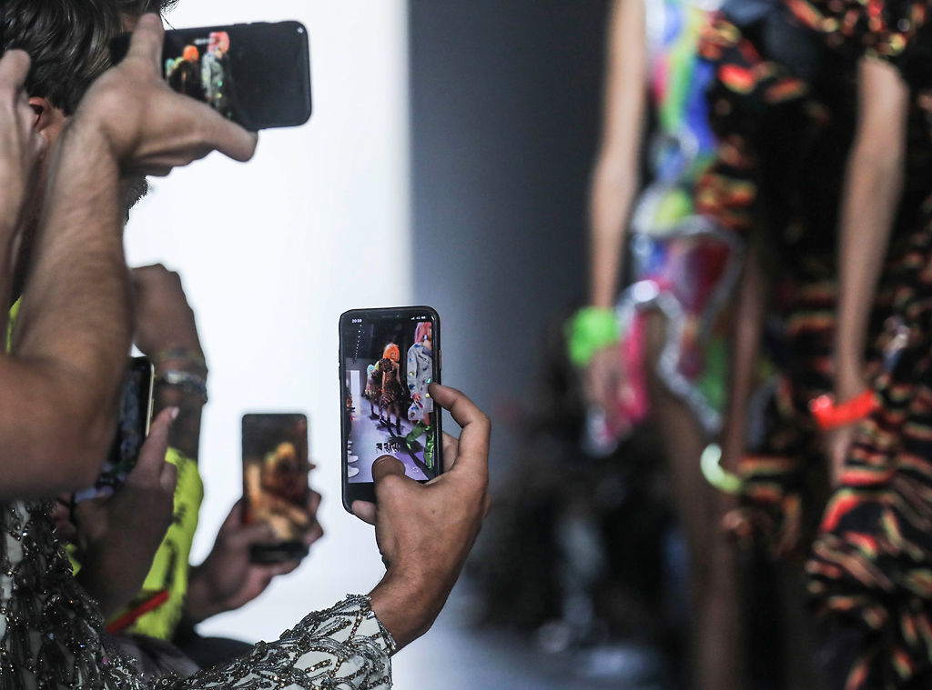Guests grab cellphone photos of models showcasing the latest fashion